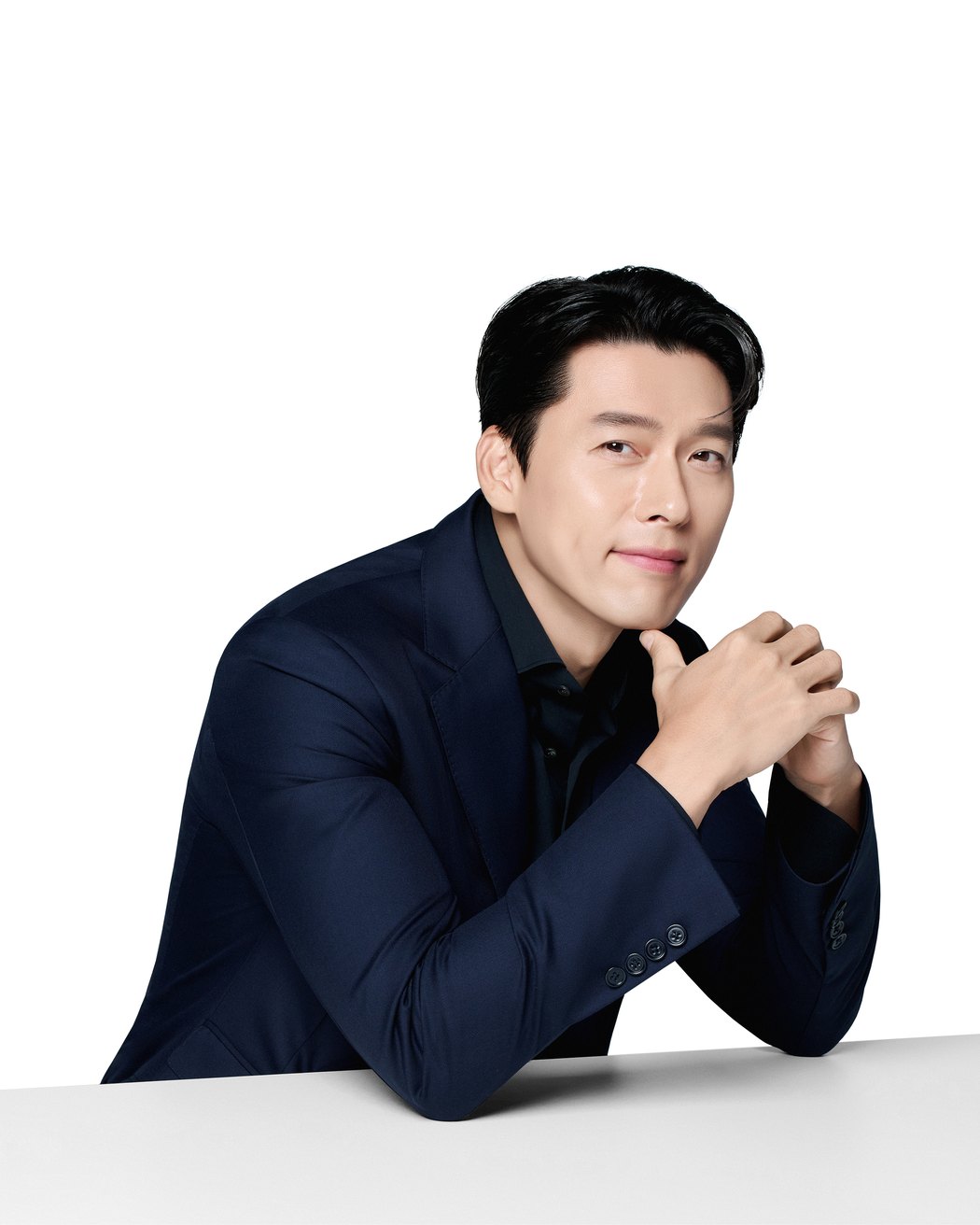 쿨소닉 전속모델 배우 현빈, 네이비 슈트 차림으로 테이블에 팔을 올리고 턱 아래로 두 손을 모은 상반신